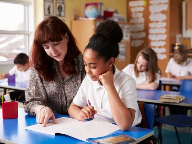White female teacher speaking with Black female student pointing at paper